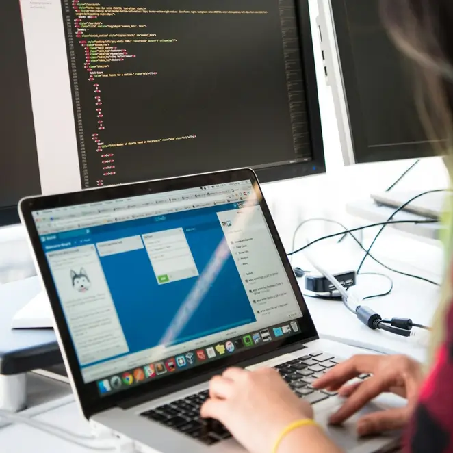 Person working on a laptop with code on two screens in the background